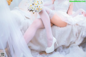 A woman in a white dress sitting on a bed.