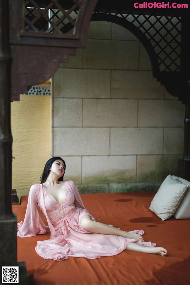 A woman in a pink dress sitting on a bed.