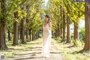 A woman in a white dress is walking down a dirt road.