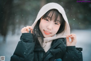 A woman standing in the snow wearing a black coat.