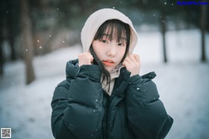 A woman standing in the snow wearing a jacket and scarf.