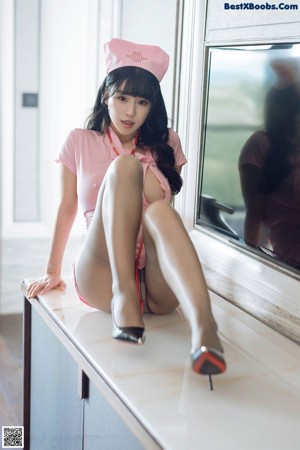 A woman in a pink nurse outfit sitting on a desk.