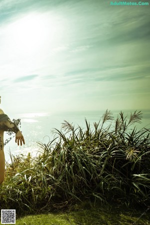 A woman in a black lingerie standing on a grassy hill overlooking the ocean.