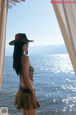A woman in a leopard print top and skirt standing by the water.