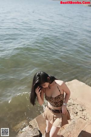 A woman in a leopard print top and skirt standing by the water.