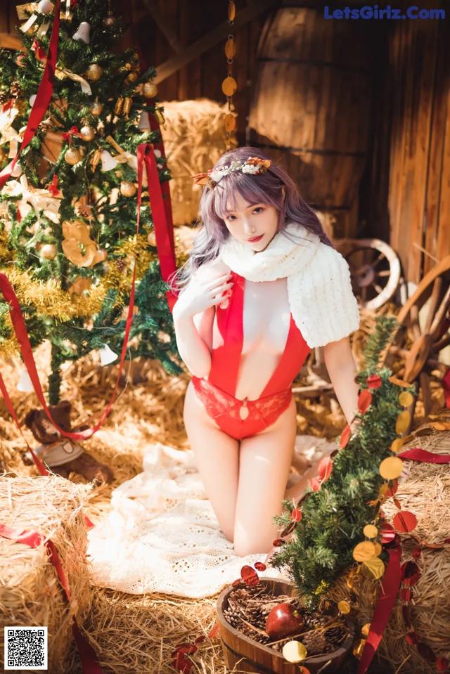 A woman in a red and white lingerie posing next to a Christmas tree.