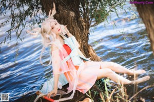 A woman sitting under a tree next to a body of water.