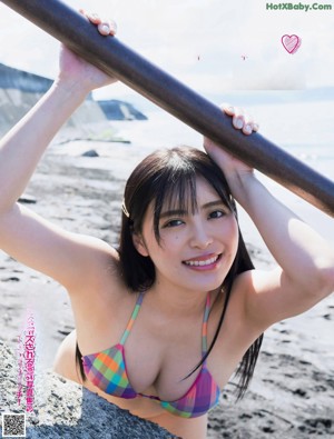 A woman in a bikini leaning against a rock on the beach.