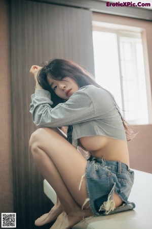 A woman in a gray shirt and white panties sitting on a bed.