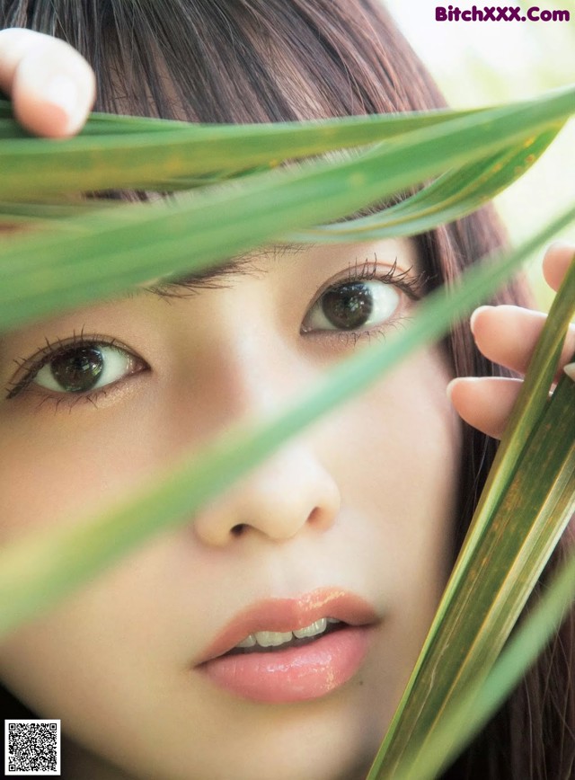 A close up of a woman's face with green leaves in front of her.