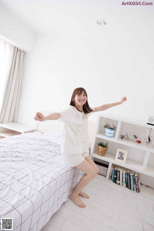 A woman standing on a bed with her arms outstretched.