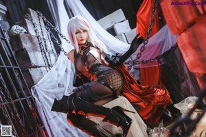 A woman in a black and red outfit sitting on a white box.