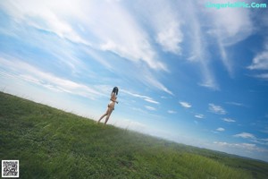 A naked woman standing on top of a lush green field.