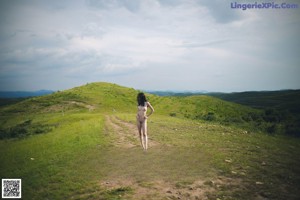 A naked woman standing on top of a lush green field.