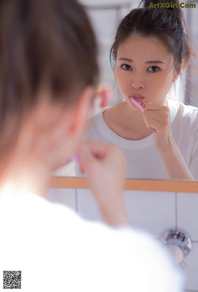 A woman brushing her teeth in front of a mirror.