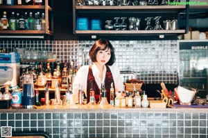 A woman standing behind a bar with bottles of alcohol.