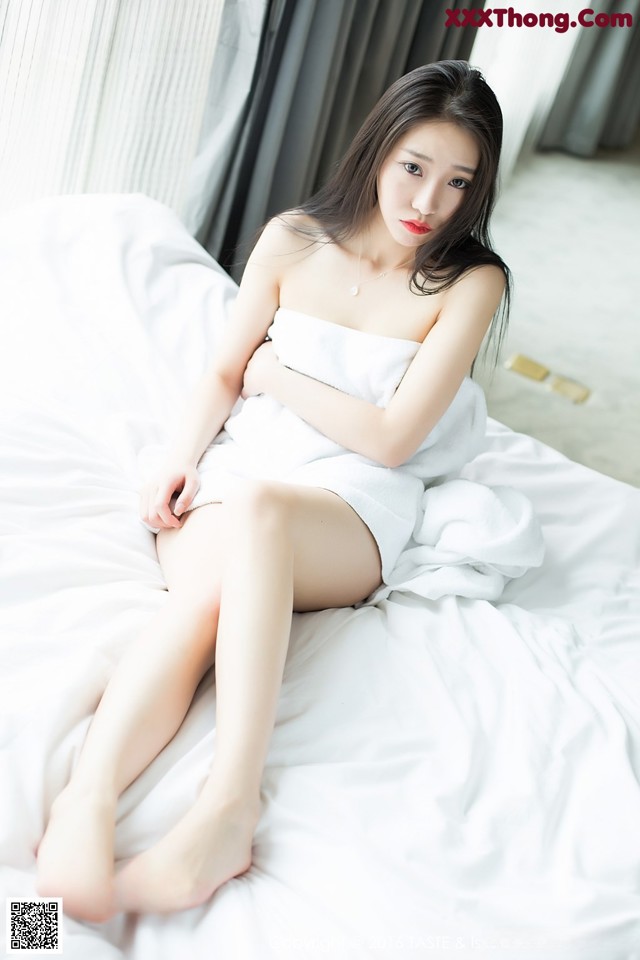 A woman in a white towel sitting on a bed.